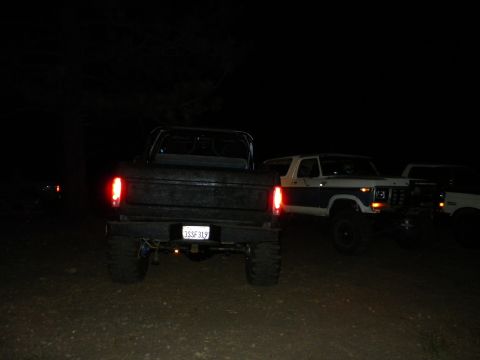 1992 Ford Bronco - Three vehicles are parked outside at night. The foreground vehicle is a black pickup truck, and a white Bronco is to its right.