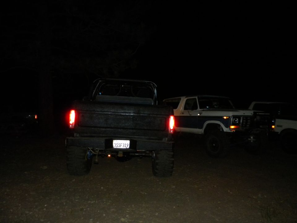 Rear view of a black pickup truck with a white Bronco and another white vehicle behind it at night. License plate reads 3SSF319