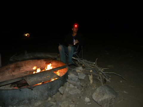 1992 Ford Bronco - A person sits in a chair next to a burning campfire, holding a drink and wearing a headlamp.