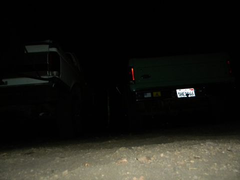 1992 Ford Bronco - Two SUVs are parked at night, with the rear of a green SUV and its license plate clearly visible.
