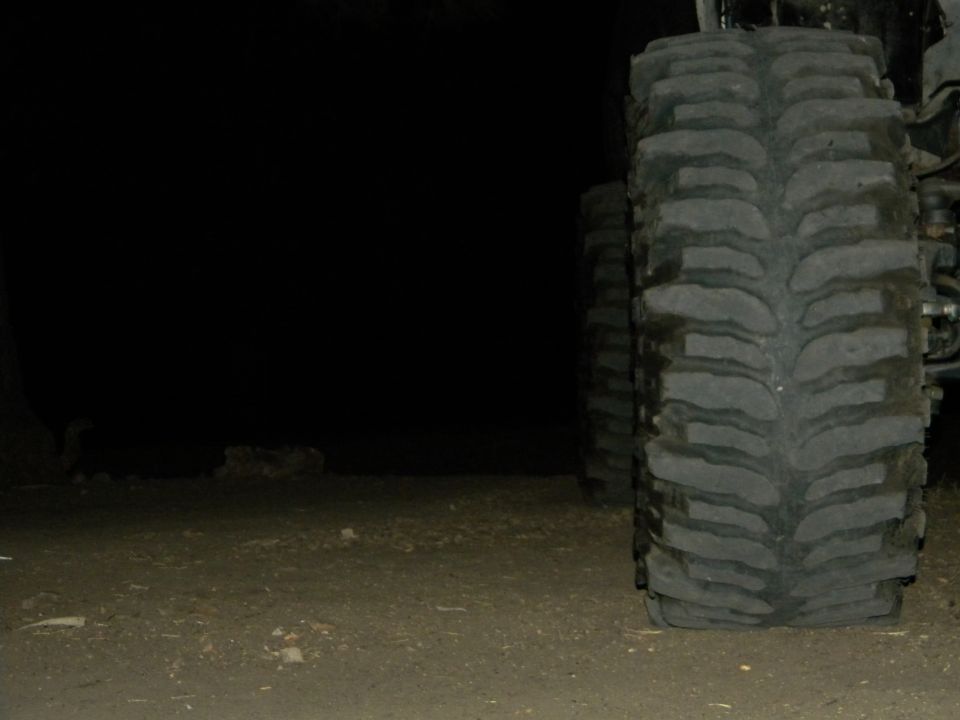 Tire tread of a large vehicle, close-up, with another tire visible behind it in the dark