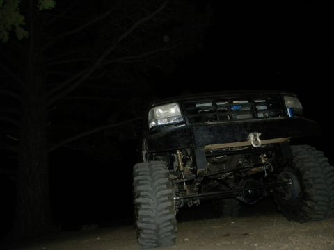 1992 Ford Bronco - A modified black Ford truck sits parked outdoors at night, its large tires and lifted suspension visible.