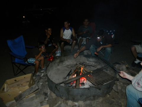 1992 Ford Bronco - Several individuals gather around a fire pit at night, with a grill grate over the coals.