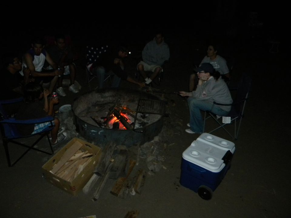 Dark scene with people gathered around objects, possibly a campfire