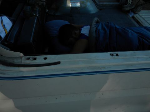 1992 Ford Bronco - Someone is sleeping in the back of a vehicle, covered by a blue blanket.