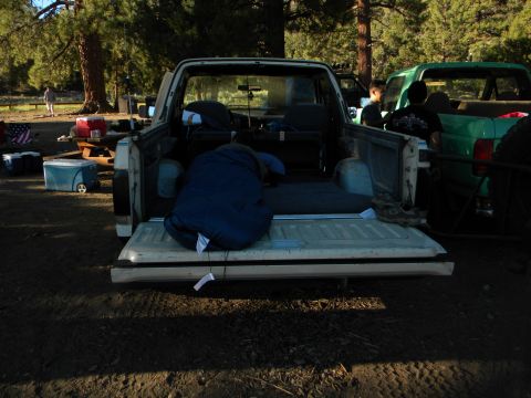 1992 Ford Bronco - A campsite scene with a pickup truck bed loaded with camping gear and another vehicle in the background.