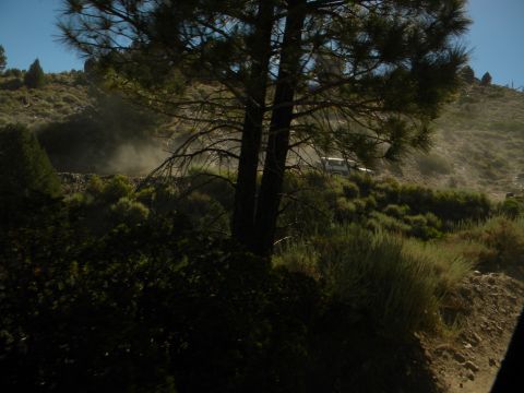 1992 Ford Bronco - A white SUV kicks up dust as it drives along a remote, hilly dirt road.