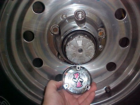 1996 Ford Bronco - A hand holds a chrome hub cap with '4x4 AUTO LOCKING' text and graphics.