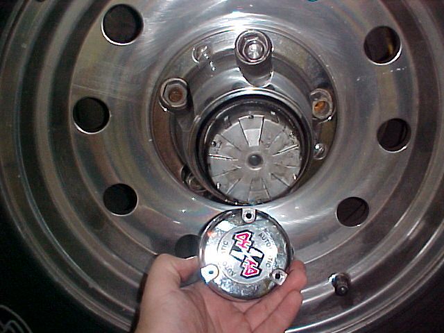 Hand holding chrome Warn hub cover in front of exposed locking hub on a steel wheel