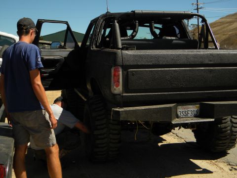 1992 Ford Bronco - A black SUV is being worked on by two people, focusing on the rear tire and suspension system.