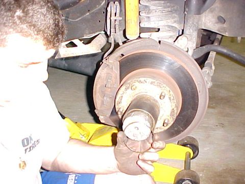 1996 Ford Bronco - A mechanic works on the brake rotor and hub of a vehicle, with a yellow jack visible.