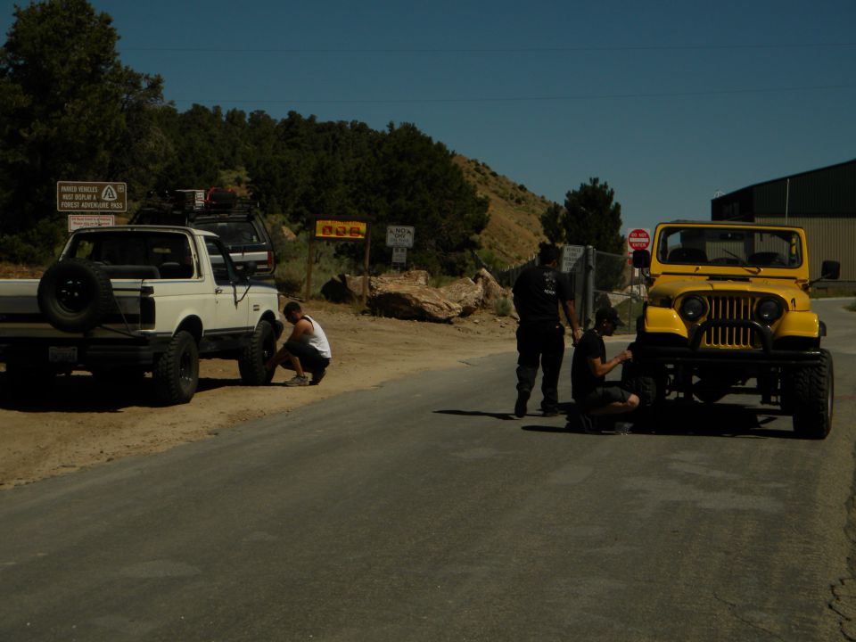 White pickup truck and yellow Jeep on a road, people working on tires