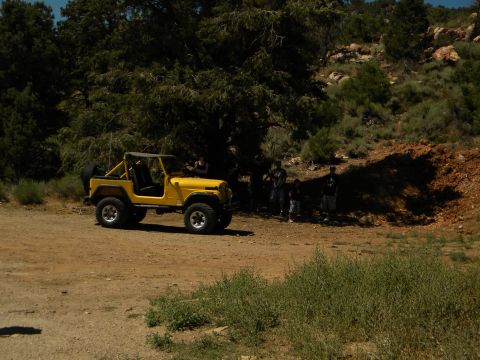 1992 Ford Bronco - A yellow Jeep CJ is parked on a dirt road near trees and hills, with several people standing nearby.