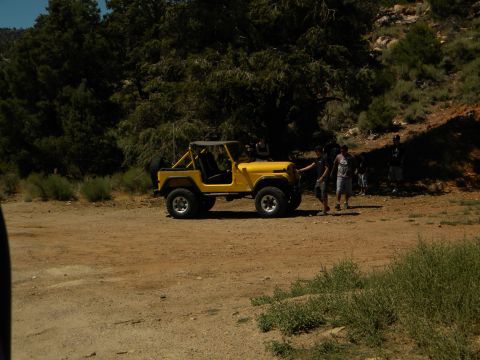 1992 Ford Bronco - A yellow Jeep CJ-5 is parked on a dirt road in a wooded area, with several people standing around it.