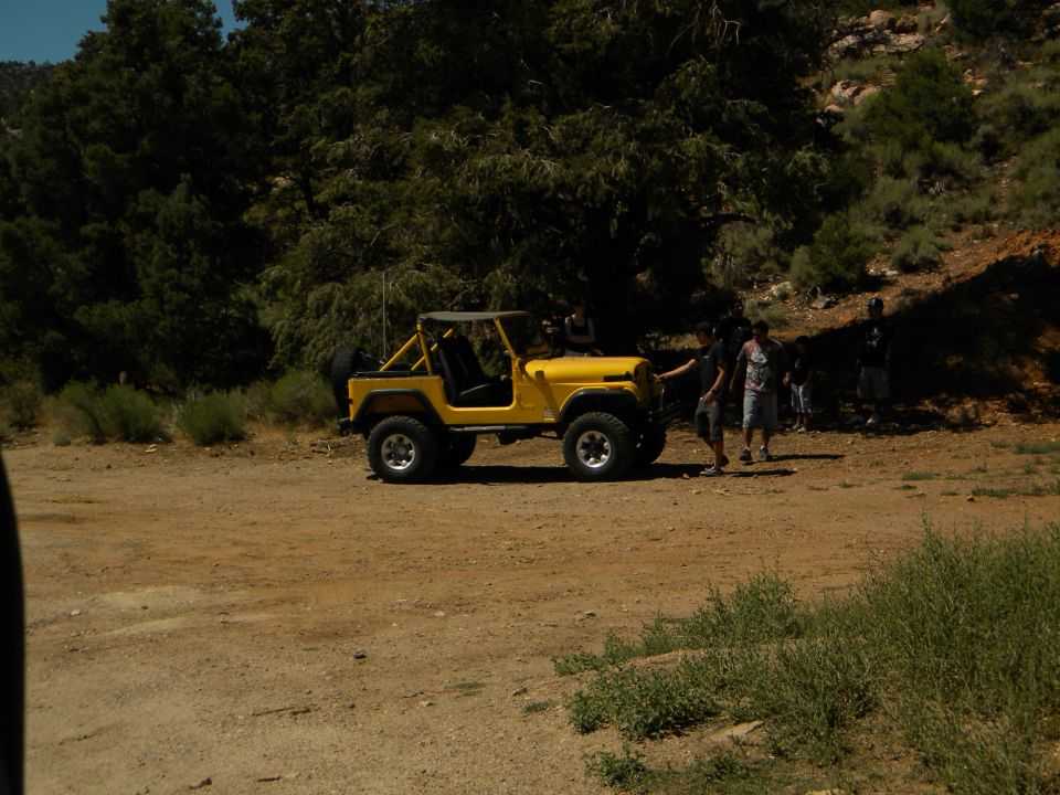 Yellow Jeep CJ-5 parked on dirt road with people nearby