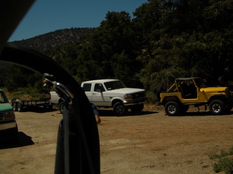 1992 Ford Bronco - Two vehicles, a white Ford truck and a yellow Jeep, are parked on a dirt road with trees in the background.