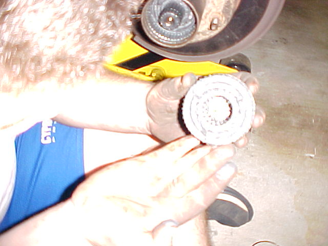 Greasy hands holding a worn cylindrical brake/bearing part near a yellow jack and brake rotor