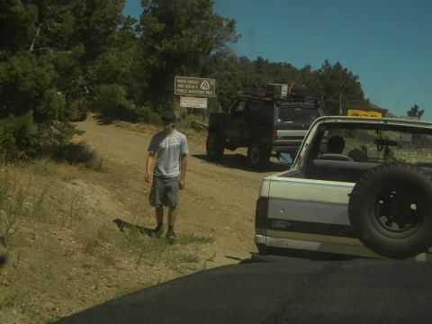 1992 Ford Bronco - A white 1992 Ford Bronco is seen from the rear, with a black SUV following on a dirt road.