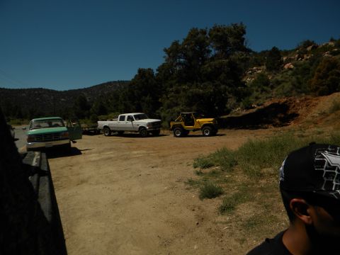 1992 Ford Bronco - Several vehicles are parked on a dusty road in a rural, hilly area under a clear blue sky.