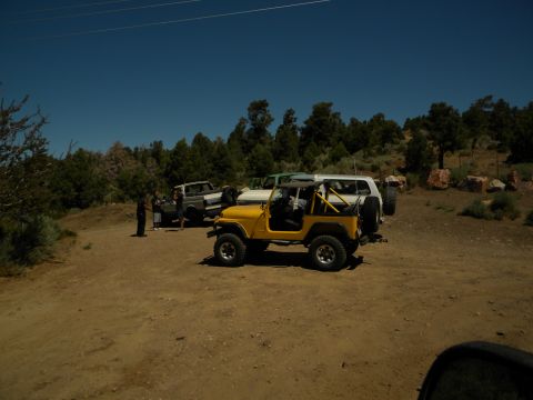 1992 Ford Bronco - Several SUVs, including a yellow Jeep CJ-7, are parked off-road on a sunny day.