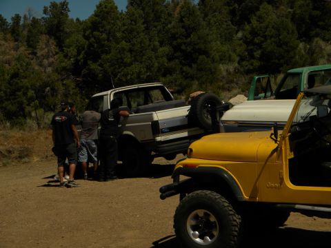 1992 Ford Bronco - Several off-road vehicles are gathered in a wooded area with a dirt ground cover.