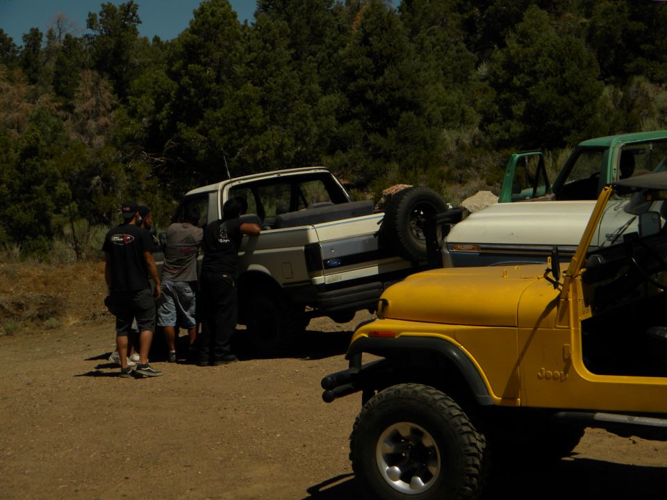 White Ford Bronco with spare tire on back, parked next to yellow Jeep CJ and green truck. People standing around