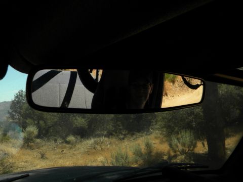 1992 Ford Bronco - Reflection in the rearview mirror shows a person and a dirt road, indicating the vehicle is in motion.