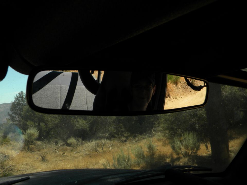 Interior rearview mirror reflection of a person and a dirt road