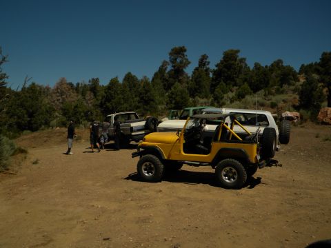 1992 Ford Bronco - A group of off-road vehicles, including a yellow Jeep Wrangler, a Ford Bronco, and a pickup truck, are parked in a dirt lot.
