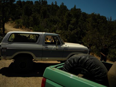 1992 Ford Bronco - A two-tone Ford Bronco, likely from the late 1970s, is parked on a dirt road with a green pickup truck in the foreground.