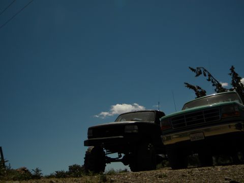 1992 Ford Bronco - Two Ford trucks, a Bronco and an F-Series, are parked on a hill, viewed from a low angle against the sky.