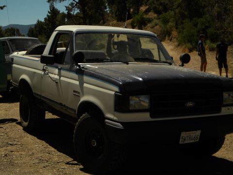 1992 Ford Bronco - This 1992 Ford Bronco is parked on a dirt road with trees and hills in the background.