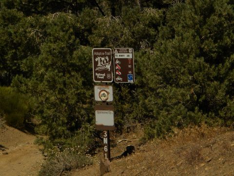 1992 Ford Bronco - A collection of trail signs, including 'Adopt-a-Trail' and directional information for HWY 18, are posted in a natural setting.
