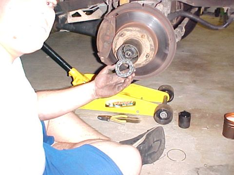 1996 Ford Bronco - A person is working on the hub assembly of a vehicle, holding a bearing race. Tools and a jack are on the floor.