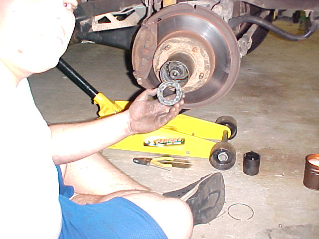 Man holding a wheel bearing beside an exposed hub and brake rotor during a front hub service