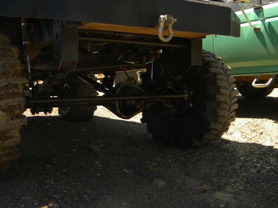 1992 Ford Bronco rear axle, suspension, and large tire, with a green vehicle in the background