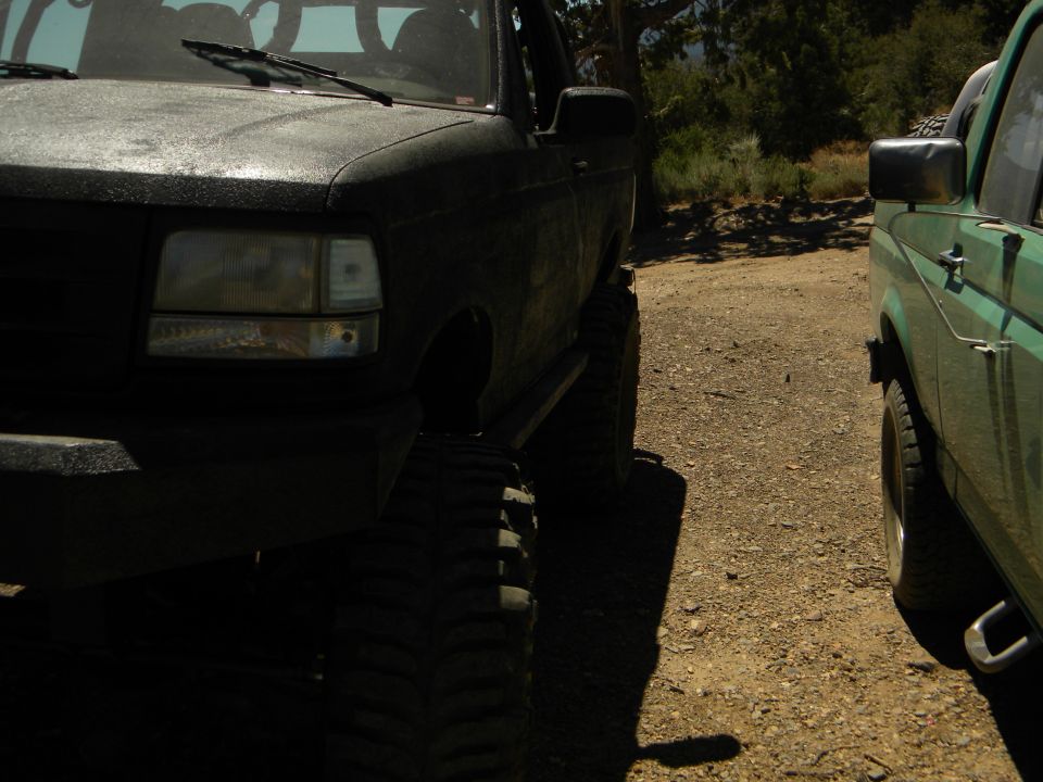 1992 Ford Bronco front quarter panel and lifted tire next to a green SUV