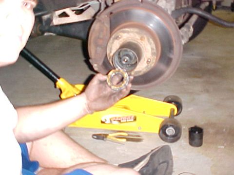 1996 Ford Bronco - A person holds a bearing while working on a vehicle's wheel hub assembly, with a yellow jack visible.
