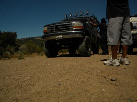 1992 Ford Bronco - A black 1992 Ford Bronco with off-road modifications is parked on a dirt lot, with another vehicle visible to the right.