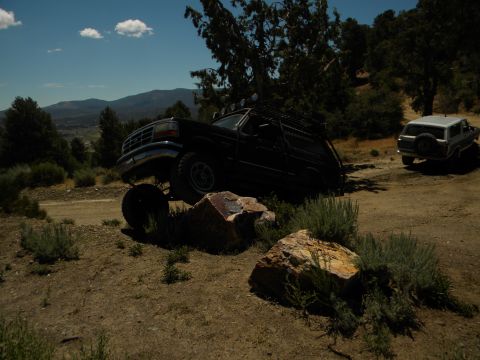 1992 Ford Bronco - Two SUVs navigate a dirt road in a hilly, wooded area under a blue sky.