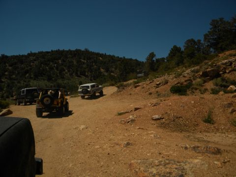 1992 Ford Bronco - A convoy of SUVs navigates a dusty mountain trail under a clear blue sky.