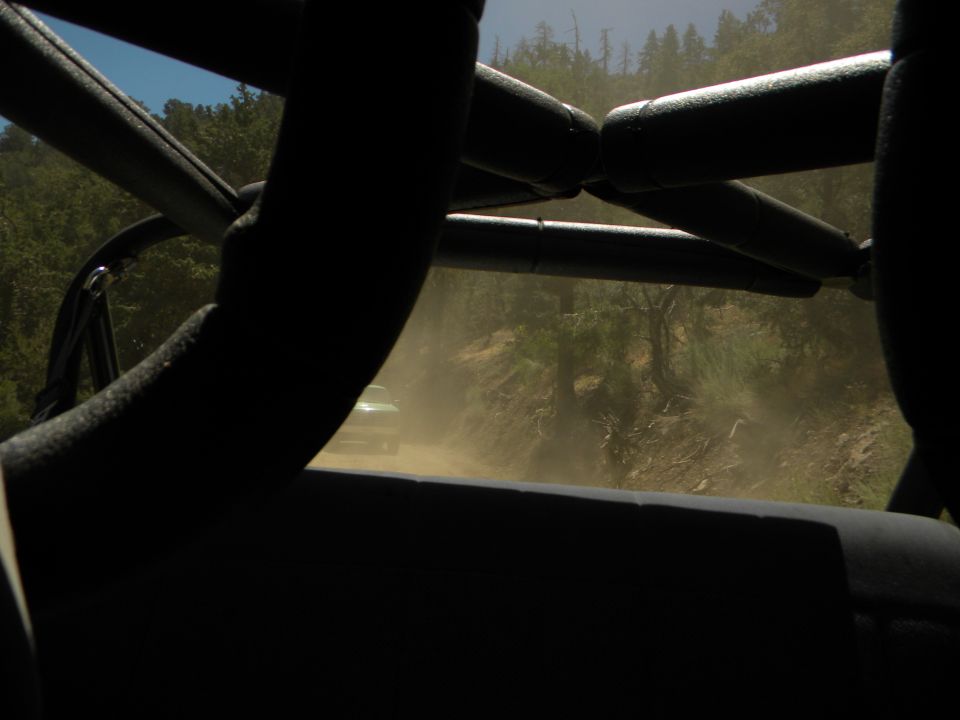 View from inside a vehicle looking out at another vehicle kicking up dust on a dirt road