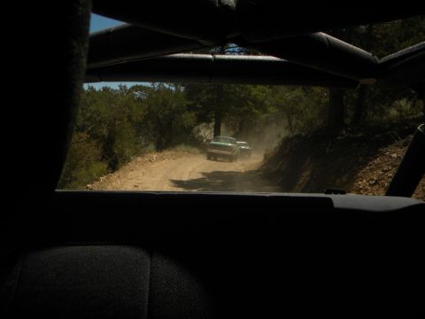 1992 Ford Bronco - View from inside a vehicle shows two trucks on a dirt road, kicking up dust.