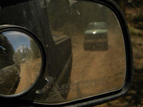 1992 Ford Bronco - A green SUV is seen in the side mirror of another vehicle on a dusty road.