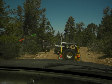 1992 Ford Bronco - Two off-road vehicles navigate a dusty trail surrounded by trees and rocky terrain.