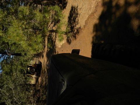 1992 Ford Bronco - A yellow tractor is visible in a wooded area next to a dirt path, with a dark vehicle in the foreground.