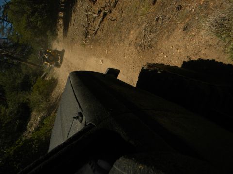 1992 Ford Bronco - Two off-road vehicles travel down a dusty dirt path through a wooded area.