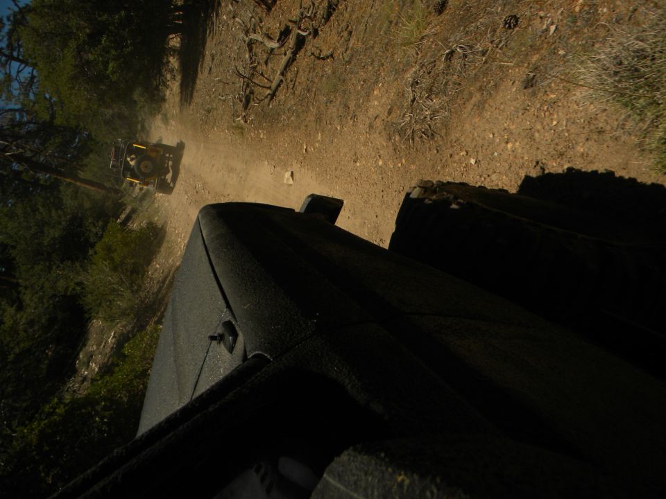 Yellow off-road vehicle kicking up dust on a dirt road, viewed from another vehicle