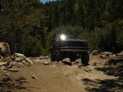 1992 Ford Bronco - 1992 Ford Bronco navigating a challenging rocky trail in a wooded area.