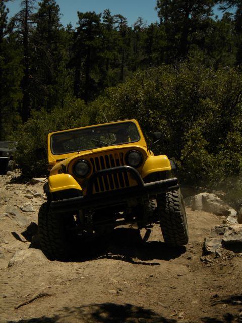 1992 Ford Bronco - A yellow Jeep CJ navigates a challenging, rocky terrain on a sunny day.
